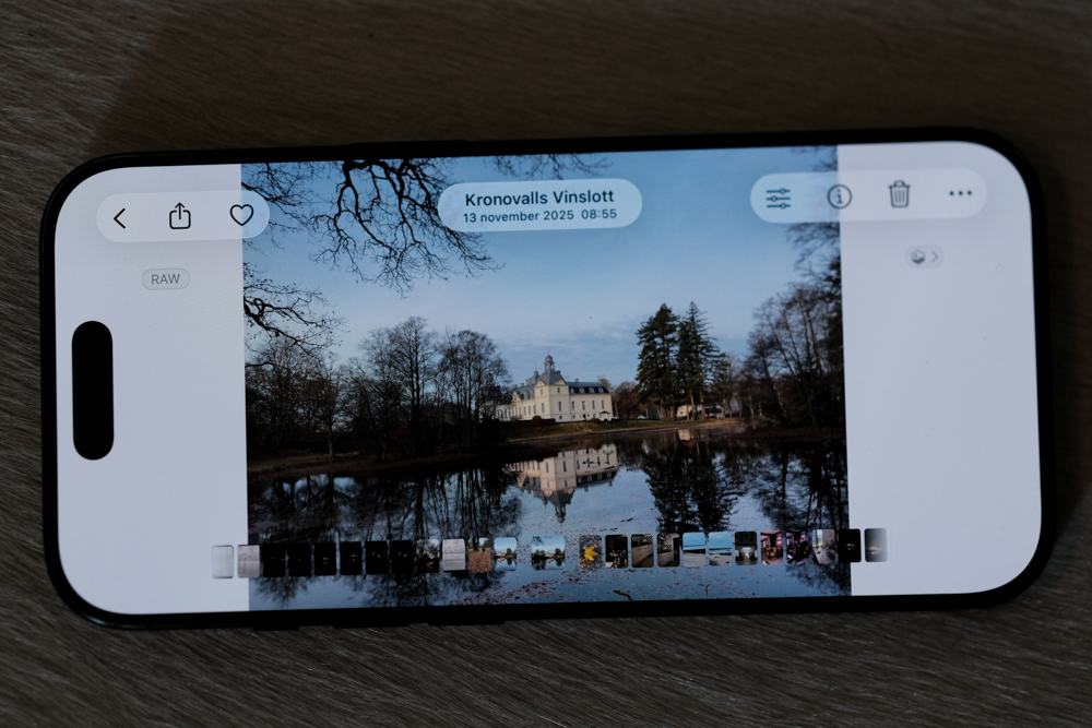 Phone screen showing a landscape photo of a white mansion by a reflective lake, in a photo editor with thumbnails along the bottom